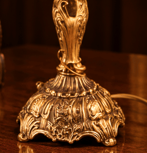 Vintage brass table lamp with an ornate base and elegant fringed velvet shade, featuring classic mid-20th-century decorative styling.