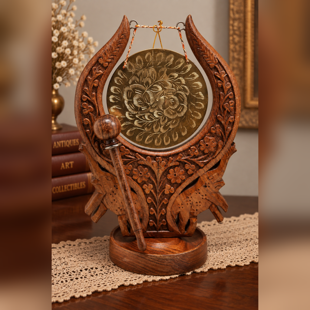 Front view of a vintage tabletop dinner gong with a hand-carved dark wood frame featuring floral designs and two elephants, holding an engraved circular brass gong with a wooden mallet.