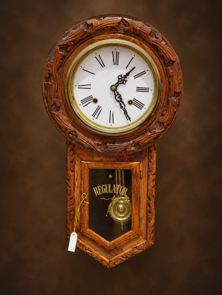 Front view of a vintage Victorian style wooden regulator wall clock with a hand-carved floral frame and a brass pendulum signed with the letter A behind stenciled glass