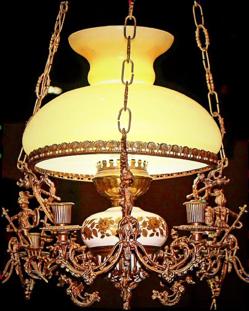 An antique 19th-century Victorian hanging oil lamp chandelier crafted from ornate gilt brass, featuring sculptural cherubs, a hand-painted floral porcelain oil font, and a large white milk glass shade.