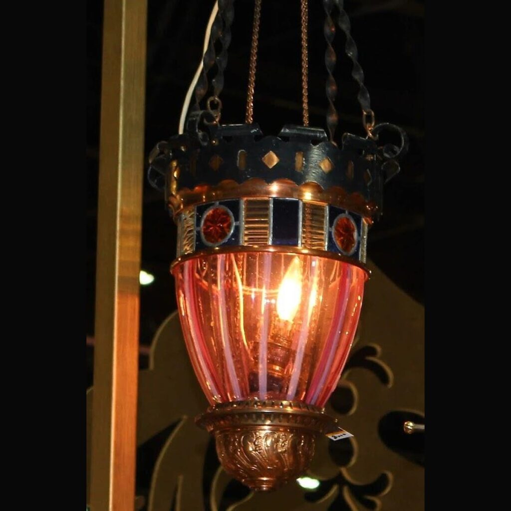 An antique c. 1900 Victorian hanging hall lantern made of ornate copper and brass, featuring a fluted pink cranberry glass body and a border of blue and gold stained glass on a dark background.