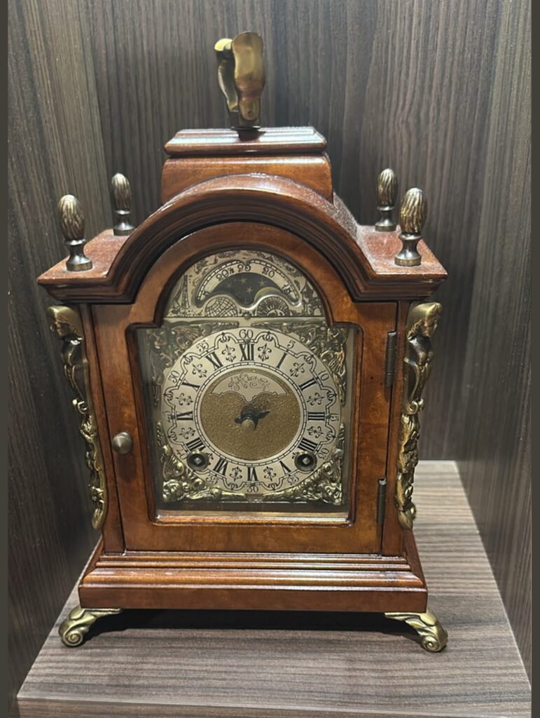 Front view of a vintage Dutch Warmink bracket mantel clock crafted from brown burr walnut with ornate gold bronze mounts and a silver moon phase dial.