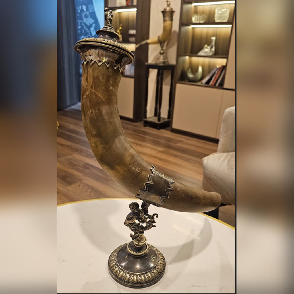 Antique 19th-century German Neo-Renaissance drinking horn centerpiece crafted from polished natural bovine horn, mounted on an ornate silver-plated cherub pedestal base, featuring a matching metal lid with a figural finial.