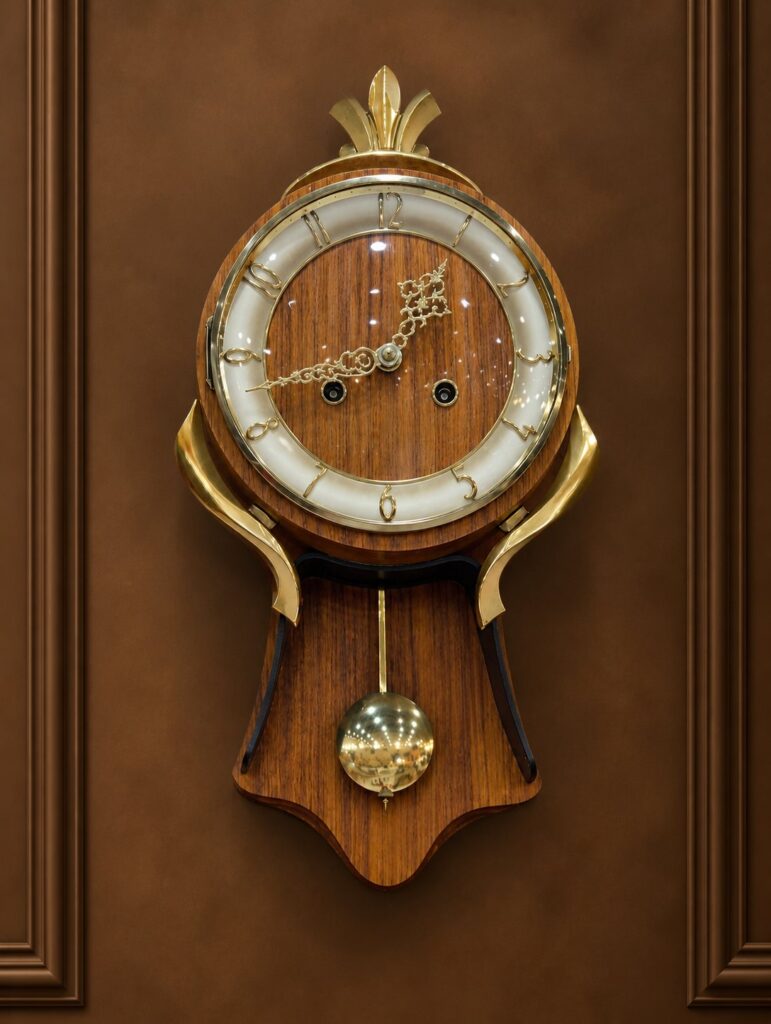 Mid-century modern vintage German Junghans Genfa wooden wall clock with a brass pendulum and ornate hands against a patterned background.