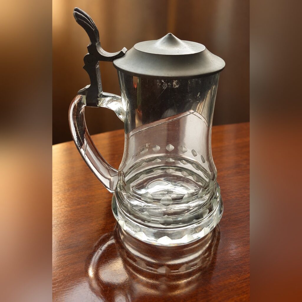 Vintage 1970s German clear glass beer stein with geometric cut patterns, heavy decorative base, glass handle, and original ornate hinged pewter lid.