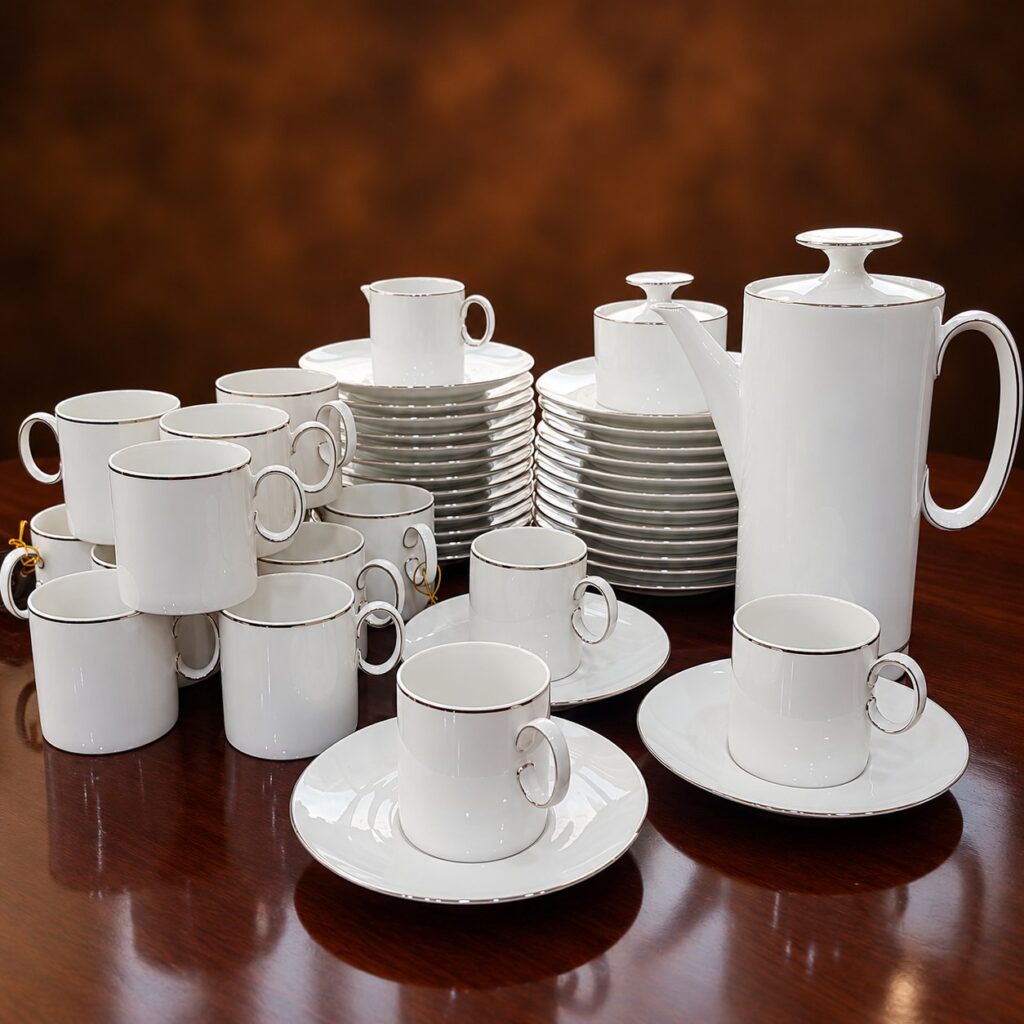 Vintage 1970s Thomas Rosenthal Germany white porcelain tea and coffee service featuring geometric cylindrical cups, circular handles, silver-trimmed saucers and plates, and a matching lidded coffee pot.