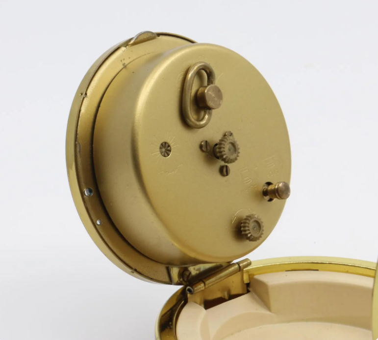 Vintage German mechanical travel alarm clock, c. 1960s, featuring a red folding clam shell case with brass-toned trim, white Arabic numeral dial and luminous-style hands.